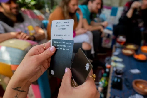 manos sosteniendo carta negra y carta blanca de mala leche con amigos en terraza jugando
