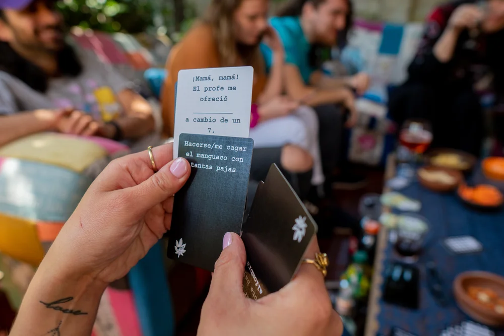 manos sosteniendo carta negra y carta blanca de mala leche con amigos en terraza jugando
